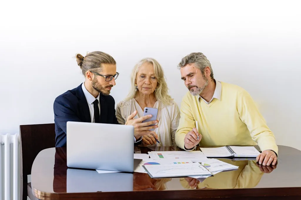 Accueil Three individuals collaborating on financial documents during a business meeting.